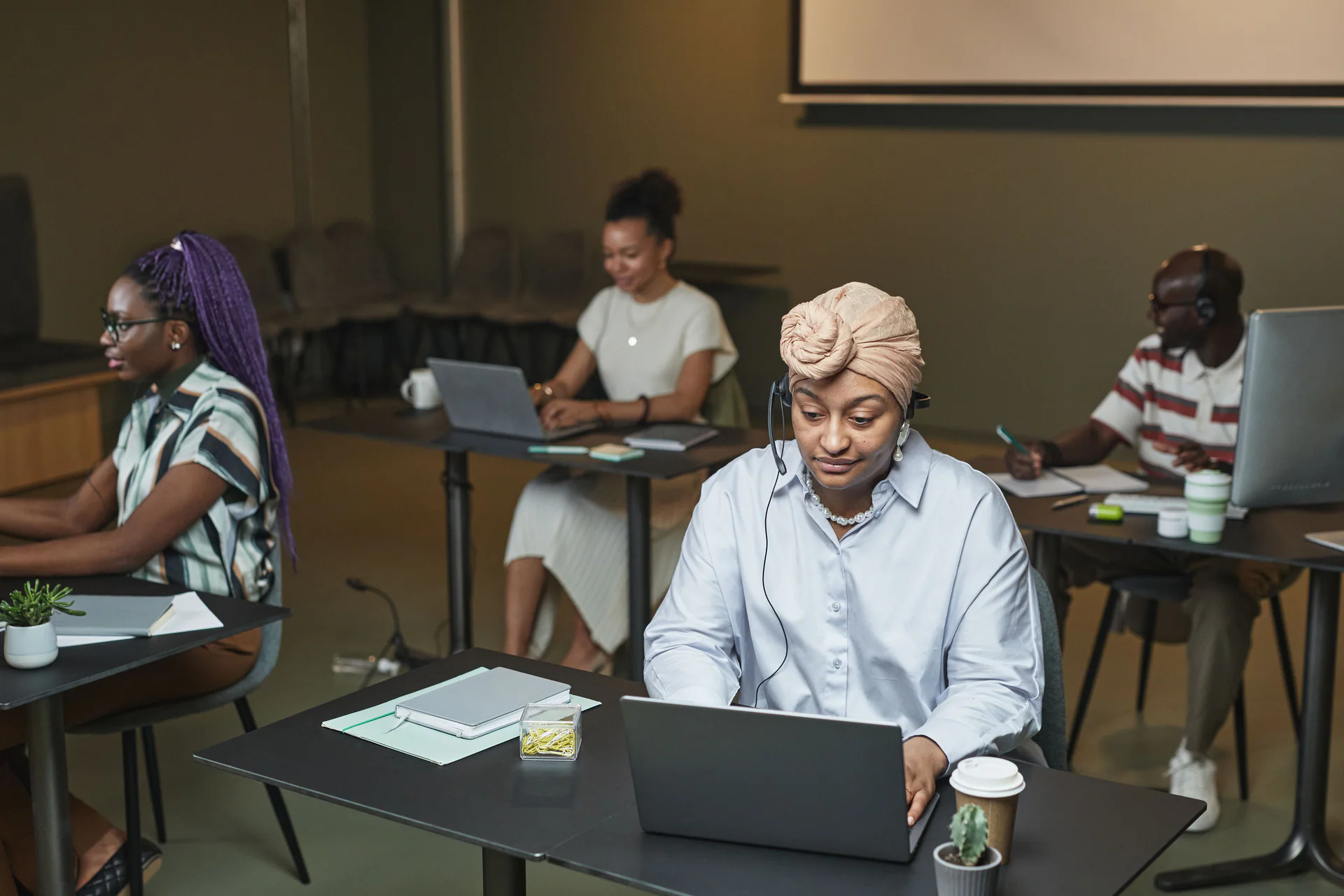 Black customer support agent working on a laptop with colleagues nearby