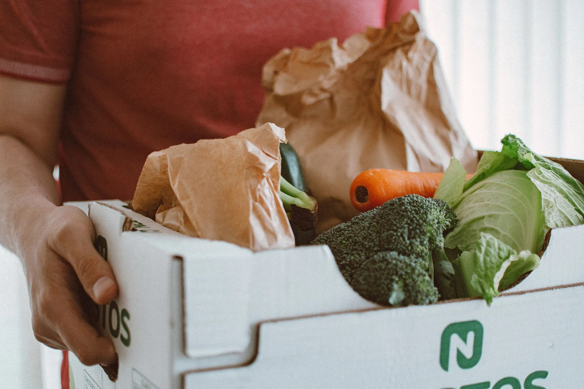 A person carrying a meal-kit style box filled with fresh vegetables